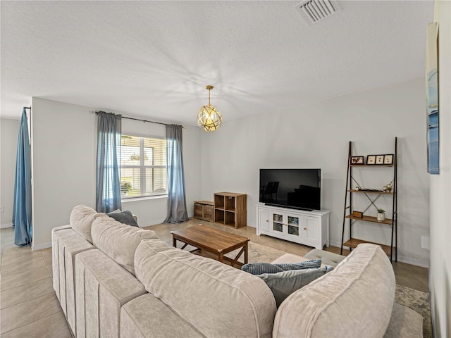 living area with a textured ceiling, a chandelier, baseboards, light tile patterned floors, and visible vents