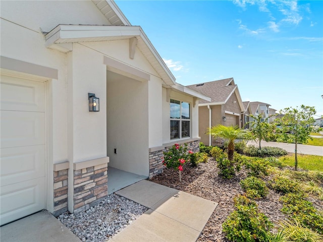 view of exterior entry with a garage, a residential view, stone siding, and stucco siding