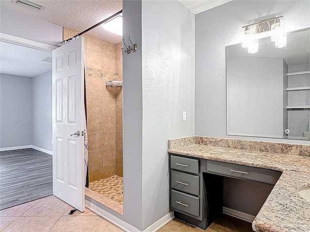 bathroom featuring visible vents, vanity, tiled shower, a textured ceiling, and tile patterned floors