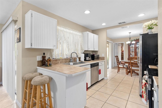 kitchen with white cabinets, light tile patterned flooring, a sink, stainless steel appliances, and a peninsula