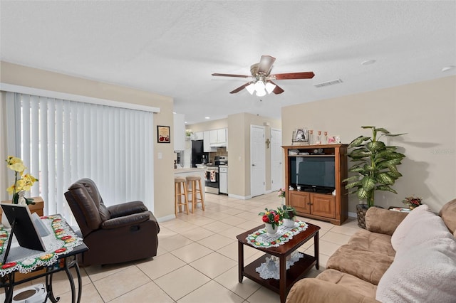 living area featuring ceiling fan, a textured ceiling, visible vents, light tile patterned floors, and baseboards