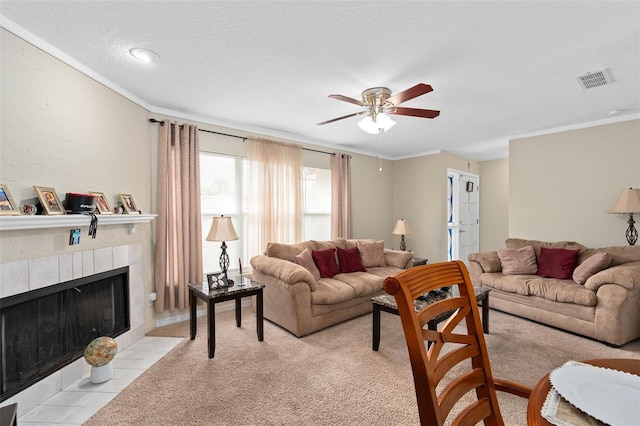 living room featuring ceiling fan, visible vents, crown molding, light colored carpet, and a tile fireplace