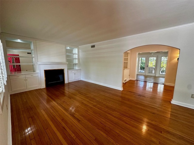 unfurnished living room featuring crown molding, arched walkways, a fireplace, baseboards, and wood-type flooring