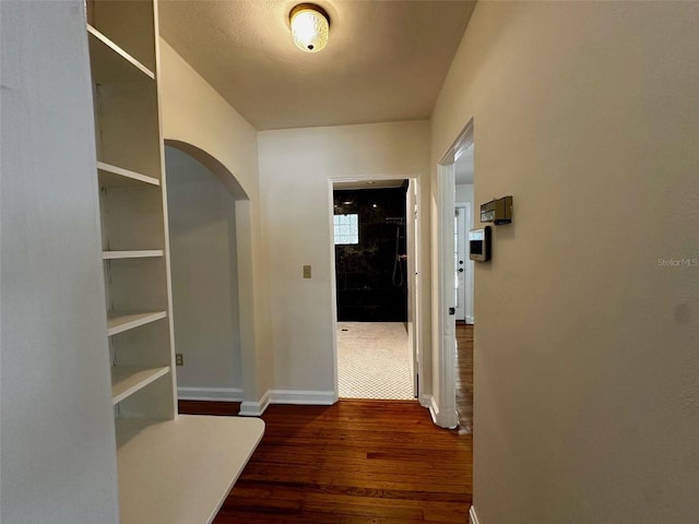 hallway with arched walkways, baseboards, and dark wood finished floors