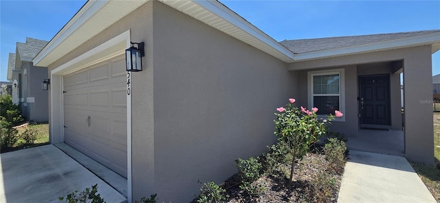 view of side of property featuring an attached garage, roof with shingles, and stucco siding