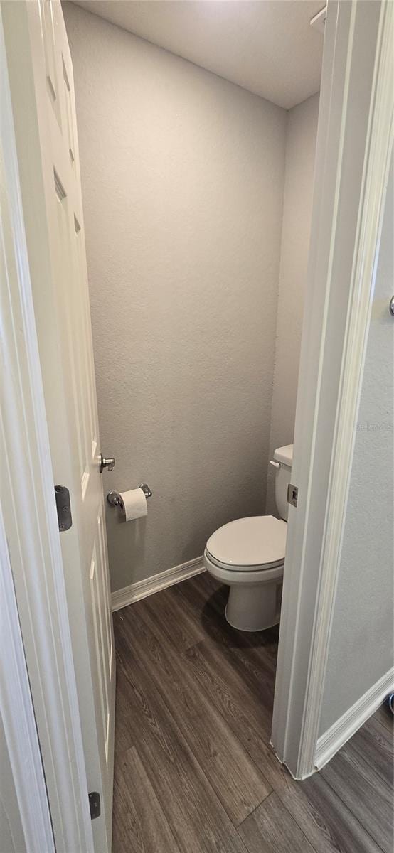 bathroom with baseboards, wood finished floors, and toilet