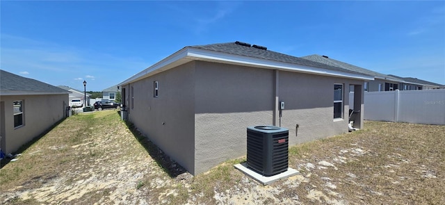 view of side of property with fence, central AC unit, and stucco siding
