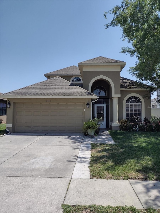 mediterranean / spanish house with a garage, a front lawn, stucco siding, and driveway