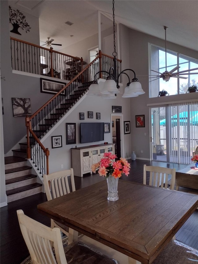 dining space with wood finished floors, baseboards, ceiling fan, a high ceiling, and stairway