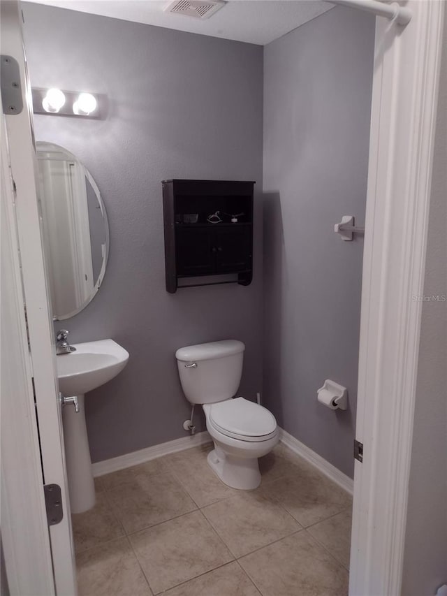 half bath featuring a sink, toilet, tile patterned floors, baseboards, and visible vents