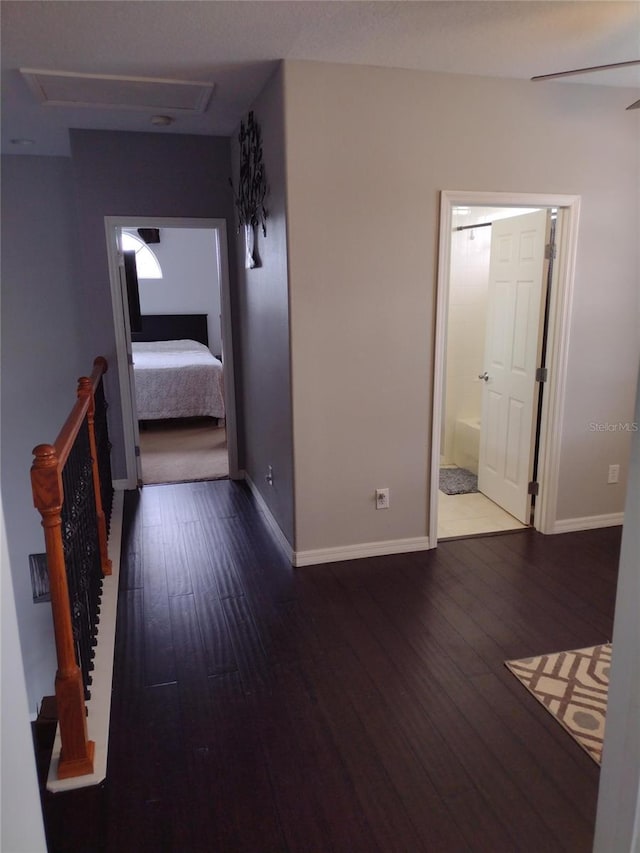 corridor featuring wood-type flooring, attic access, and baseboards