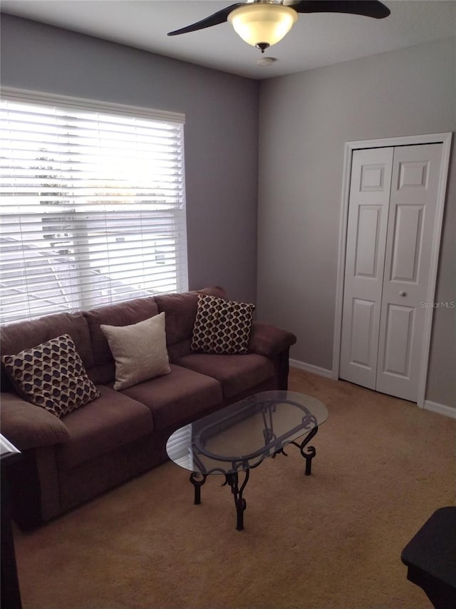 living area featuring baseboards, a ceiling fan, and light colored carpet