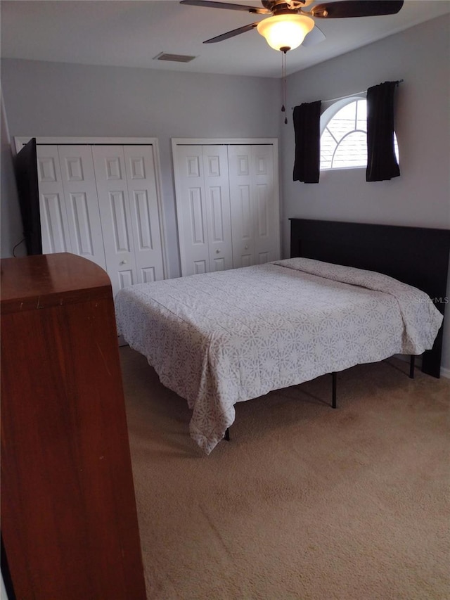 carpeted bedroom featuring multiple closets, ceiling fan, and visible vents