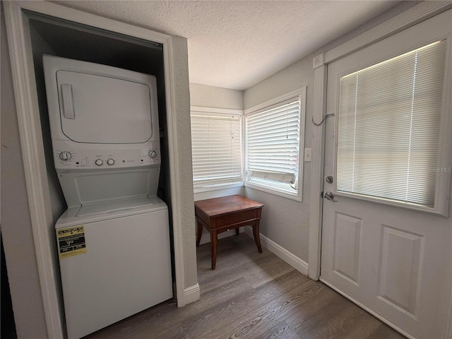 laundry area with laundry area, a textured ceiling, stacked washer / drying machine, wood finished floors, and baseboards