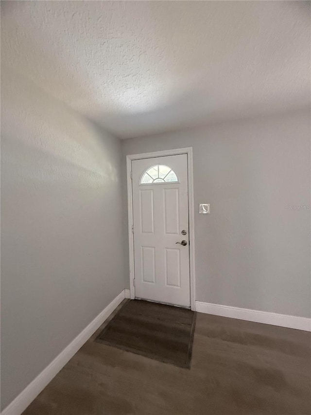 doorway to outside featuring baseboards, a textured ceiling, and dark wood-style floors