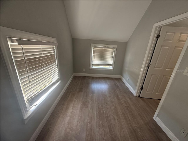 empty room featuring baseboards, vaulted ceiling, and dark wood-type flooring