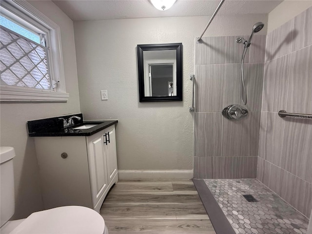 full bathroom featuring toilet, a tile shower, wood finished floors, and vanity