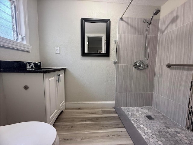 bathroom featuring vanity, toilet, tiled shower, and wood finished floors