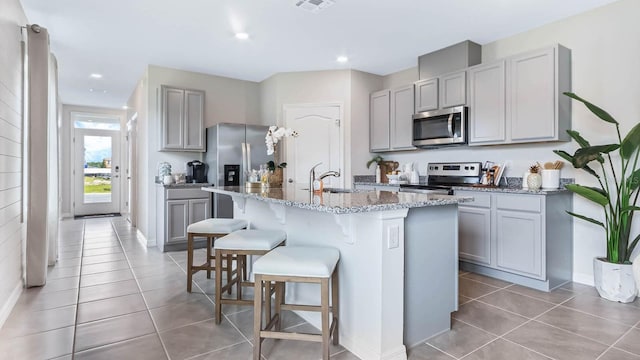 kitchen featuring light stone countertops, appliances with stainless steel finishes, gray cabinetry, and a breakfast bar