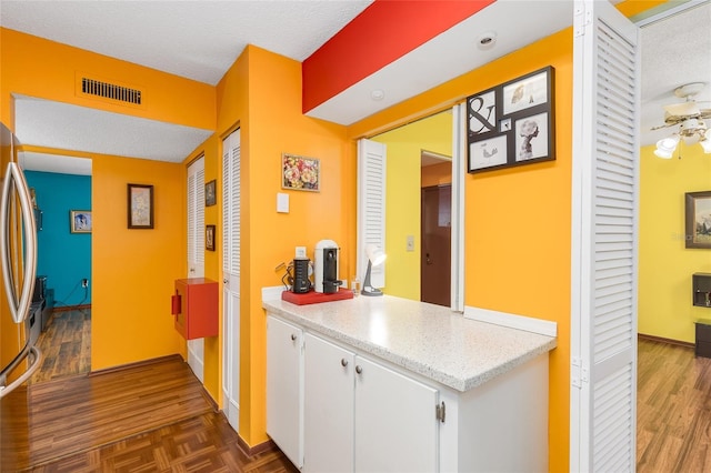 hallway featuring baseboards, parquet floors, a textured ceiling, and visible vents