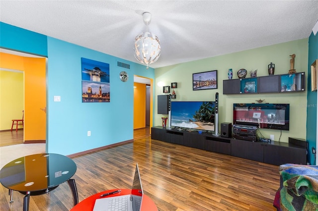 living area featuring a textured ceiling, a notable chandelier, wood finished floors, and visible vents