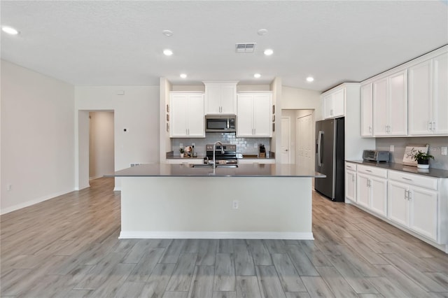 5347 Travertine St, Mount Dora, FL 32757 - kitchen with stainless steel appliances, light wood finished floors, decorative backsplash, dark countertops, and a center island with sink