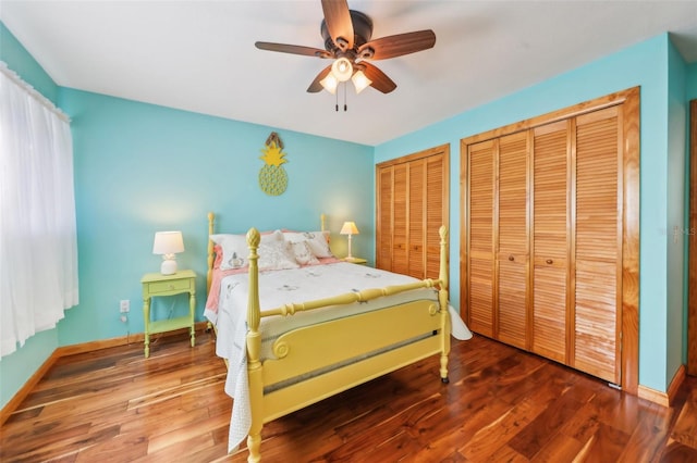 bedroom featuring wood finished floors, a ceiling fan, baseboards, and two closets