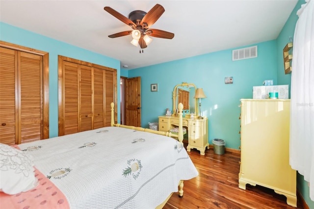 bedroom featuring a ceiling fan, visible vents, wood finished floors, baseboards, and multiple closets