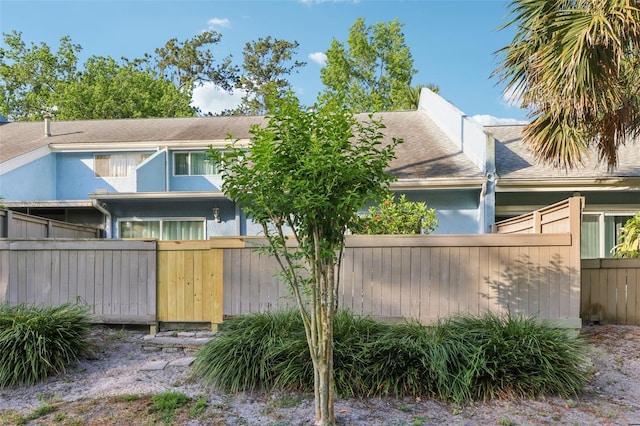 rear view of house featuring fence and a shingled roof