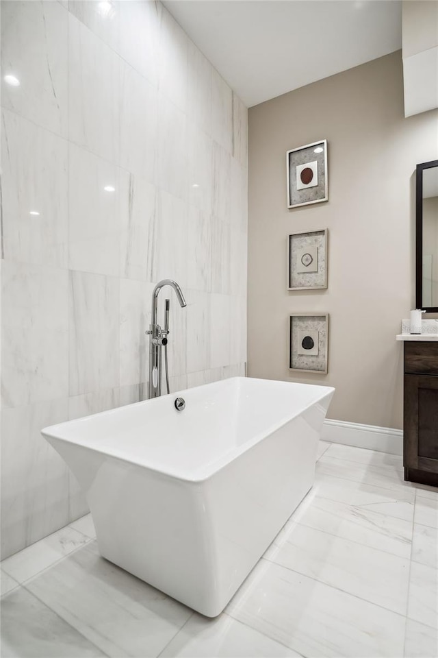 full bath with vanity, marble finish floor, a freestanding tub, and tile walls