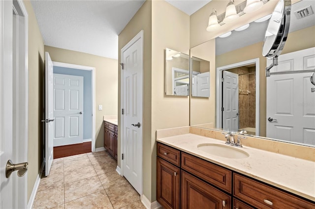 bathroom featuring visible vents, a tile shower, vanity, baseboards, and tile patterned floors