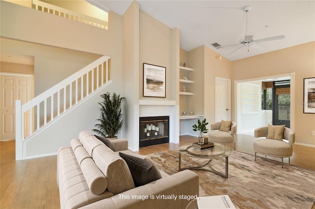 living area featuring ceiling fan, built in features, wood finished floors, baseboards, and stairs