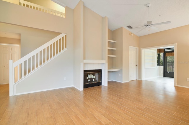 unfurnished living room with built in features, baseboards, ceiling fan, stairway, and light wood-type flooring