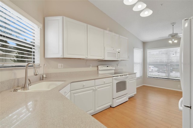 kitchen with a sink, white cabinetry, vaulted ceiling, and white appliances