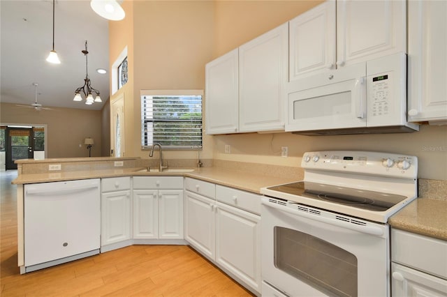 kitchen with a towering ceiling, white appliances, ceiling fan, a sink, and light wood-style flooring
