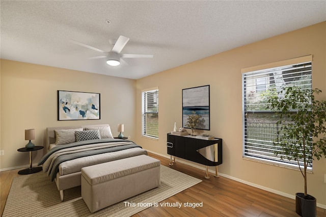 bedroom with baseboards, a textured ceiling, multiple windows, and wood finished floors