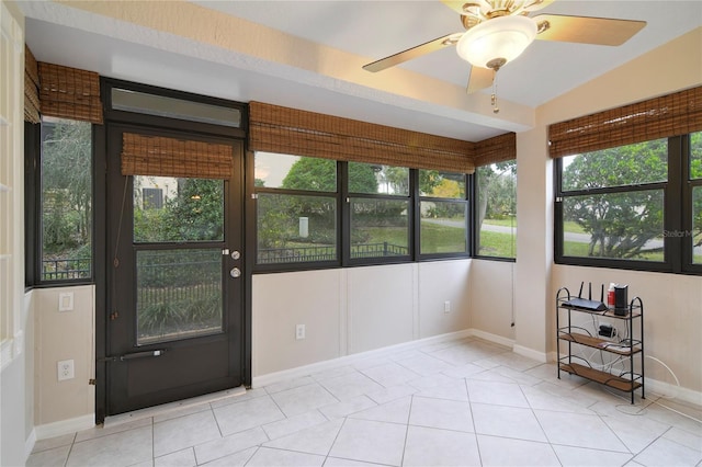 unfurnished sunroom with a ceiling fan, baseboards, and tile patterned flooring