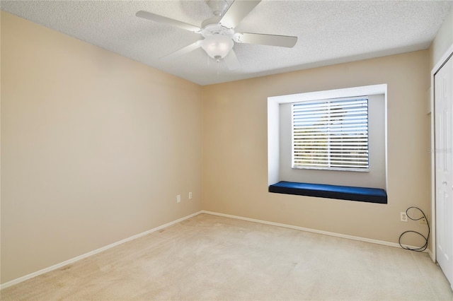 empty room with baseboards, a ceiling fan, a textured ceiling, and light carpet