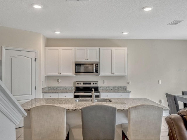 3033 Beau Loop, Tavares, FL 32778 - kitchen featuring stainless steel appliances, light stone countertops, a center island with sink, and light tile patterned floors