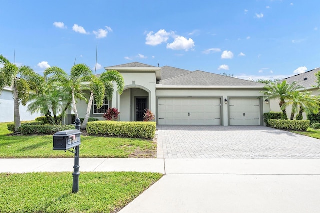 single story home featuring decorative driveway, a front lawn, an attached garage, a shingled roof, and stucco siding