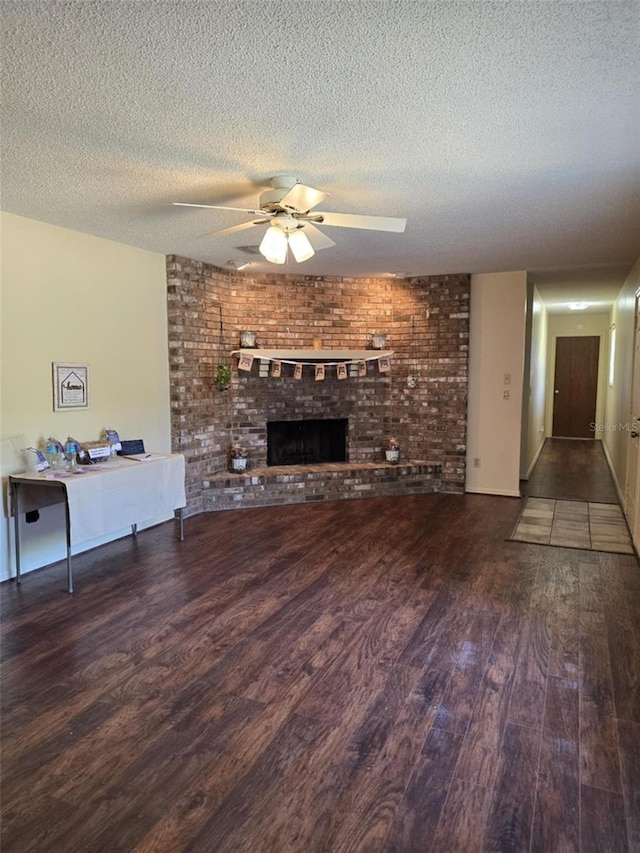 unfurnished living room featuring a ceiling fan, a textured ceiling, a brick fireplace, and wood finished floors