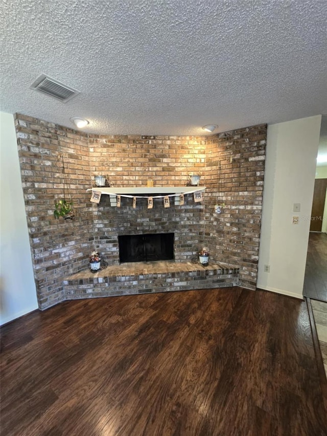 unfurnished living room featuring visible vents, a textured ceiling, wood finished floors, and a fireplace