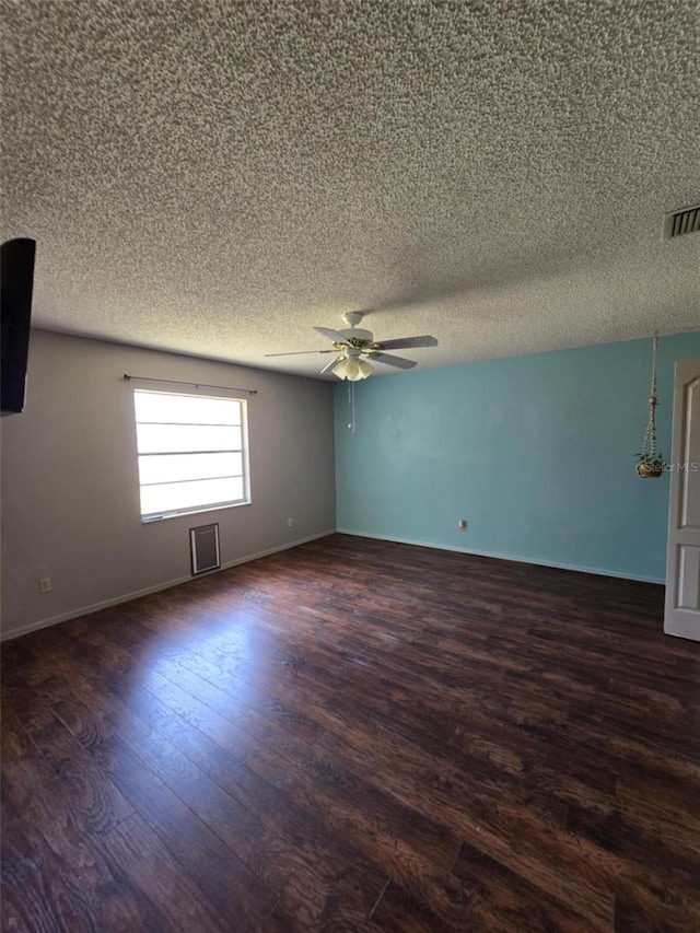 empty room featuring visible vents, a ceiling fan, dark wood finished floors, and a textured ceiling