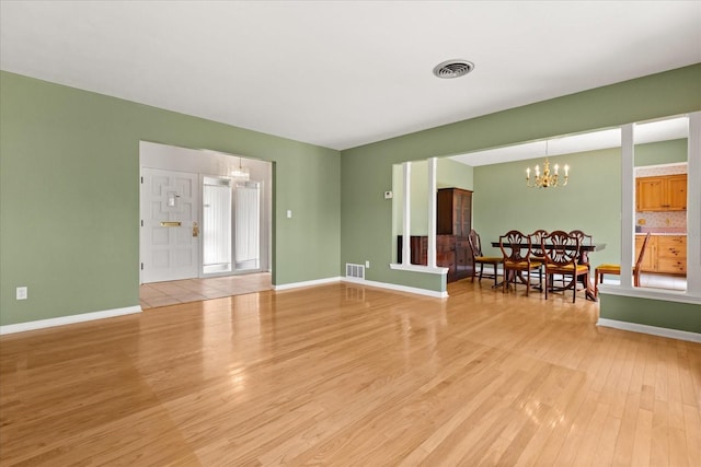 living area with baseboards, an inviting chandelier, light wood-style flooring, and visible vents