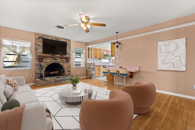 living room with a ceiling fan, visible vents, a fireplace, baseboards, and light wood finished floors