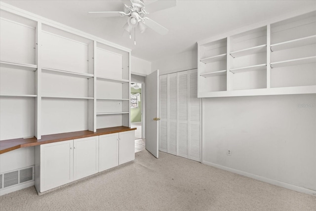 interior space with built in study area, light carpet, a ceiling fan, and visible vents