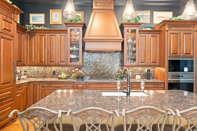 9730 Lounsberry Cir, Golden Oak, FL 32836 - kitchen featuring appliances with stainless steel finishes, custom range hood, backsplash, brown cabinetry, and crown molding