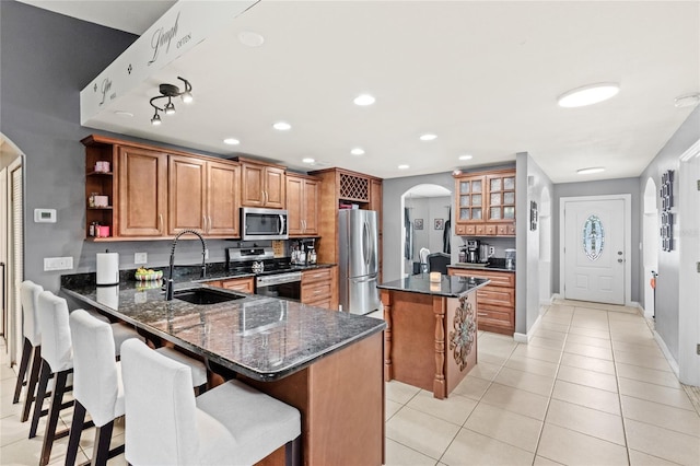 kitchen with appliances with stainless steel finishes, a center island, arched walkways, brown cabinets, and a sink