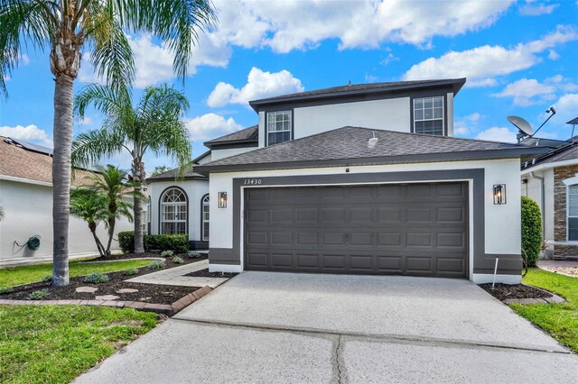traditional-style home with a garage, roof with shingles, stucco siding, and concrete driveway