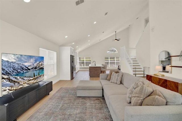 living room featuring ceiling fan, visible vents, high vaulted ceiling, light wood-style floors, and recessed lighting